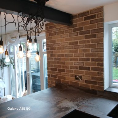 Warm brick slip kitchen feature wall in Flitwick with pendant lights and a dark ceiling beam